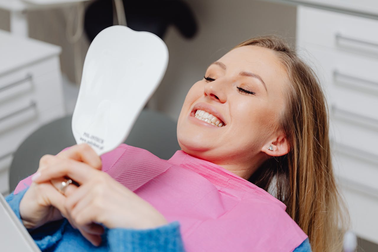 Crafting Captivating Headlines: Your awesome post title goes here A woman at a dental clinic smiles while holding a mirror, showcasing her dental treatment results.